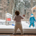 baby stands in front of window in the winter