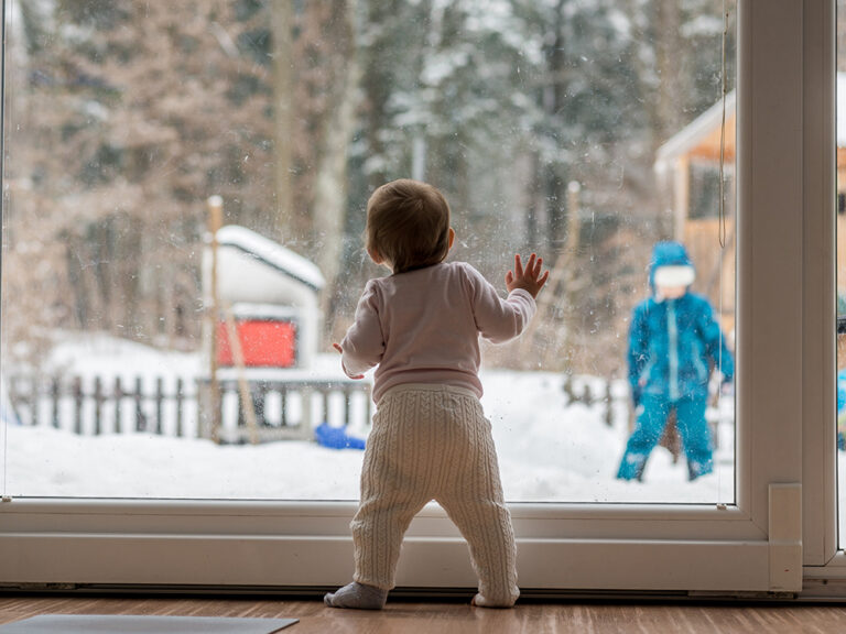 baby stands in front of window in the winter