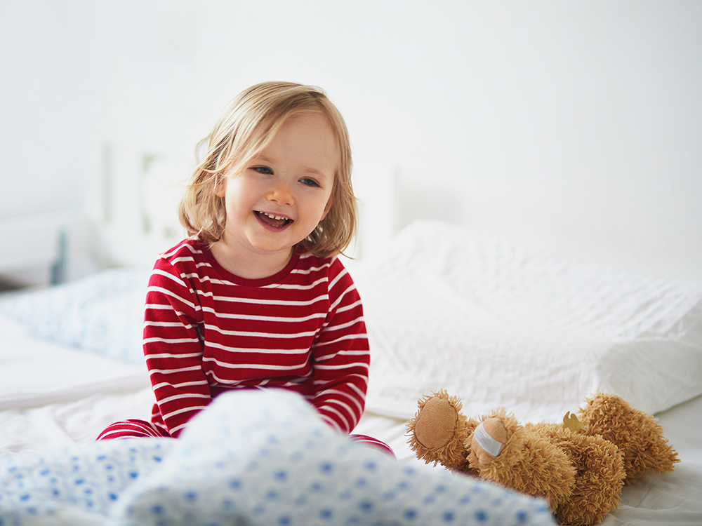 little girl sitting on bed in pajamas with teddy